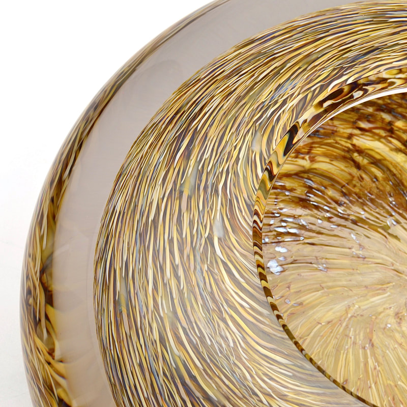A close up view of a thick, optical glass bowl with amber and gold murrini.
